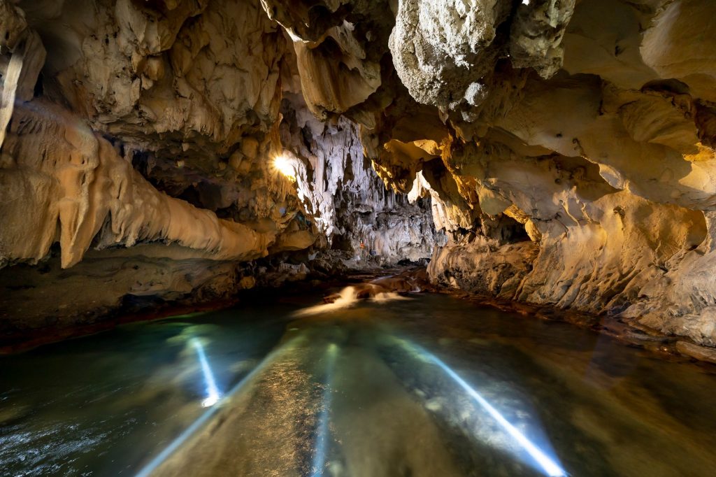 Caverna subterrânea com formações rochosas e um rio de águas tranquilas