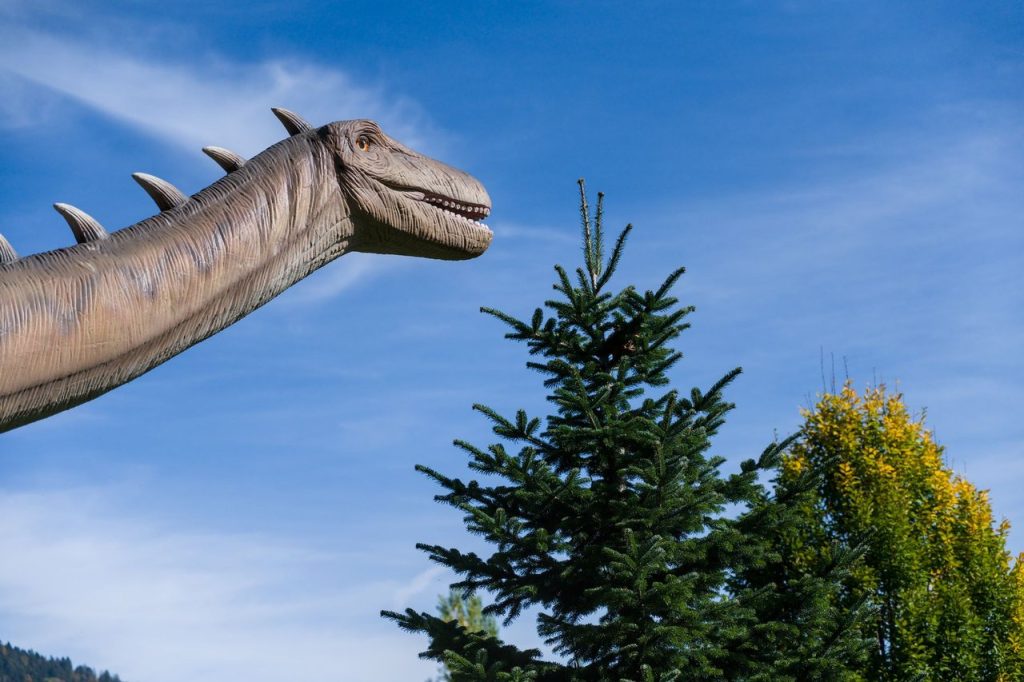 Fóssil encontrado em obra no Maranhão revela novo dinossauro gigante ligado à Europa Escultura de dinossauro em tamanho real ao ar livre, diante de árvores e do céu azul.