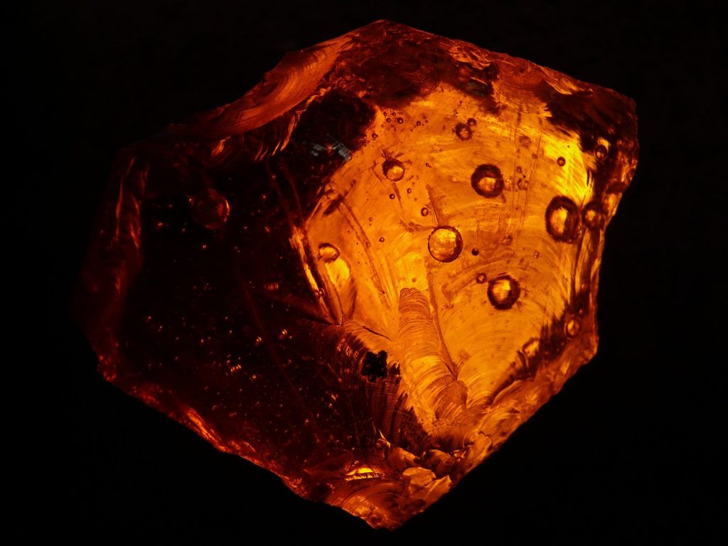 Pedra de âmbar alaranjada em close, com texturas e padrões internos visíveis.