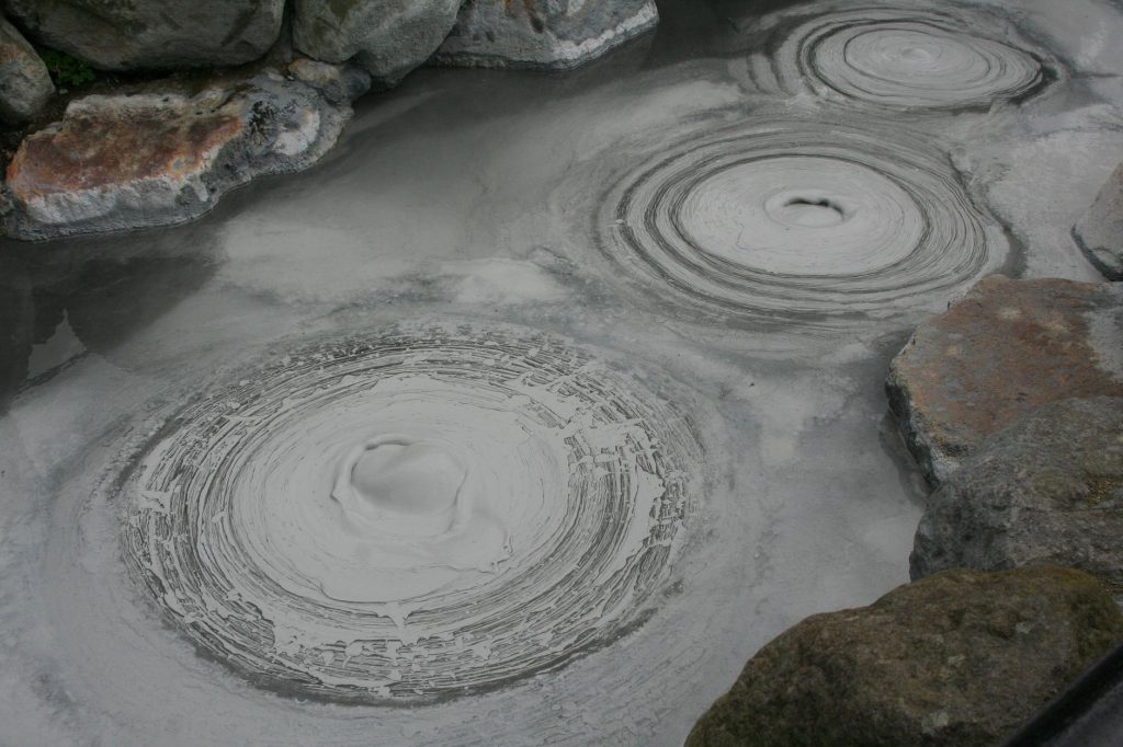 Poças de lama borbulhantes em uma área geotérmica, com vapor emergindo da superfície.